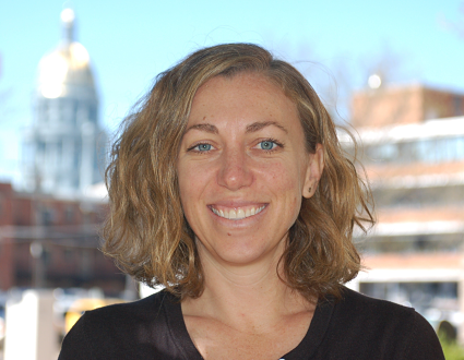 Woman with wavy shoulder-length hair smiling at camera with cityscape background