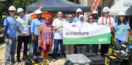 Group of people in hard hats holding an Accenture banner at a community construction event