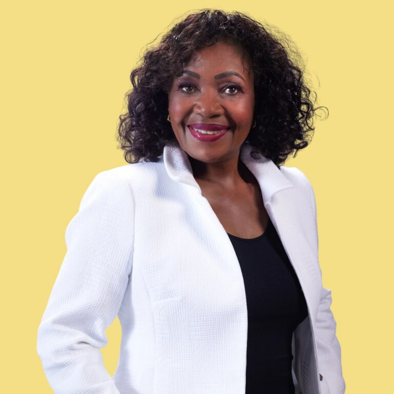 Professional headshot of Phyllis Currie wearing a white blazer against a yellow background