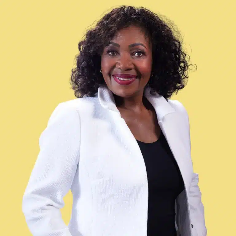 Professional headshot of Phyllis Currie wearing a white blazer against a yellow background