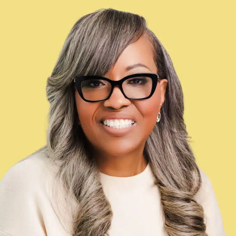 Smiling woman with gray hair and glasses against yellow background