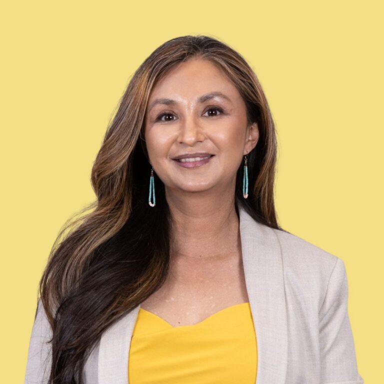 Collette Brown-Rodriguez, woman with long brown hair wearing yellow top and beige blazer against yellow background