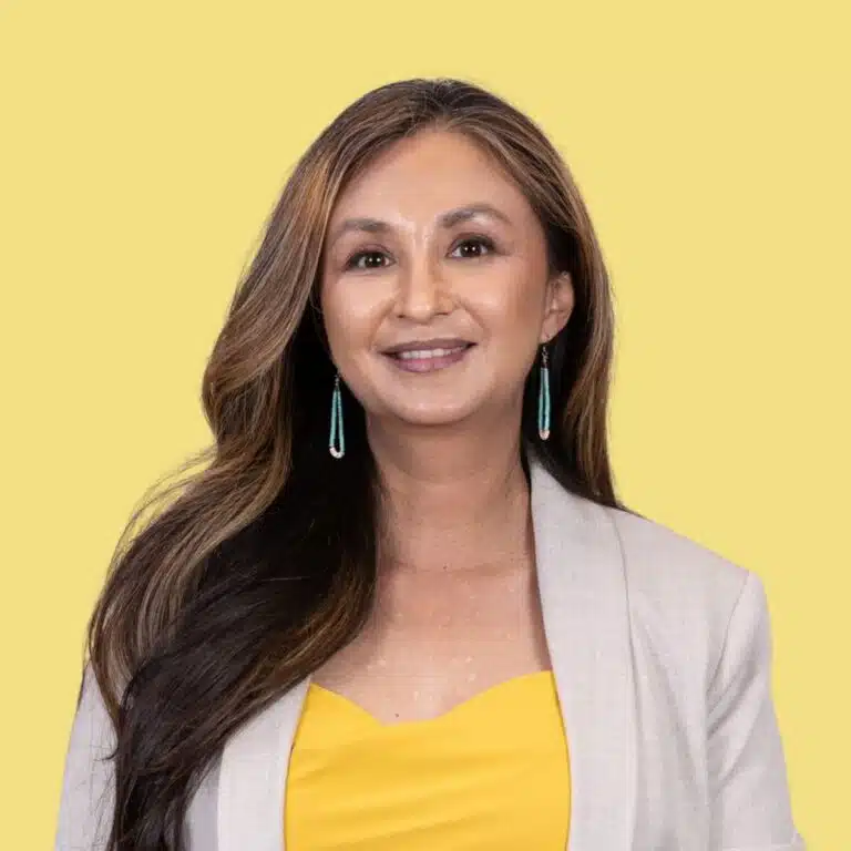 Collette Brown-Rodriguez, woman with long brown hair wearing yellow top and beige blazer against yellow background