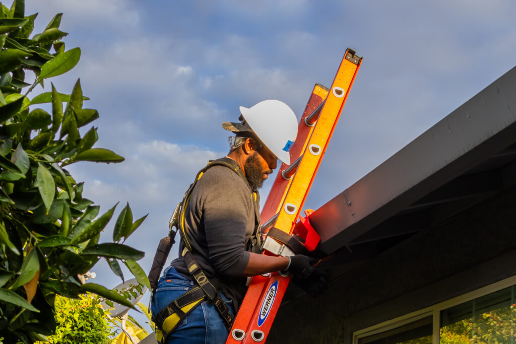 Construction worker on ladder carrying red level against building exterior