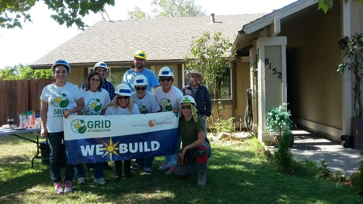 GRID Alternatives volunteer team in hard hats holding "We Build" banner outside home