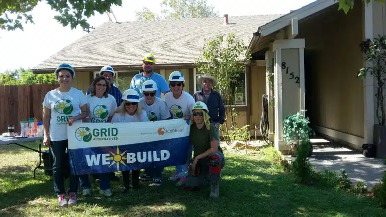 GRID Alternatives volunteer team in hard hats holding "We Build" banner outside home