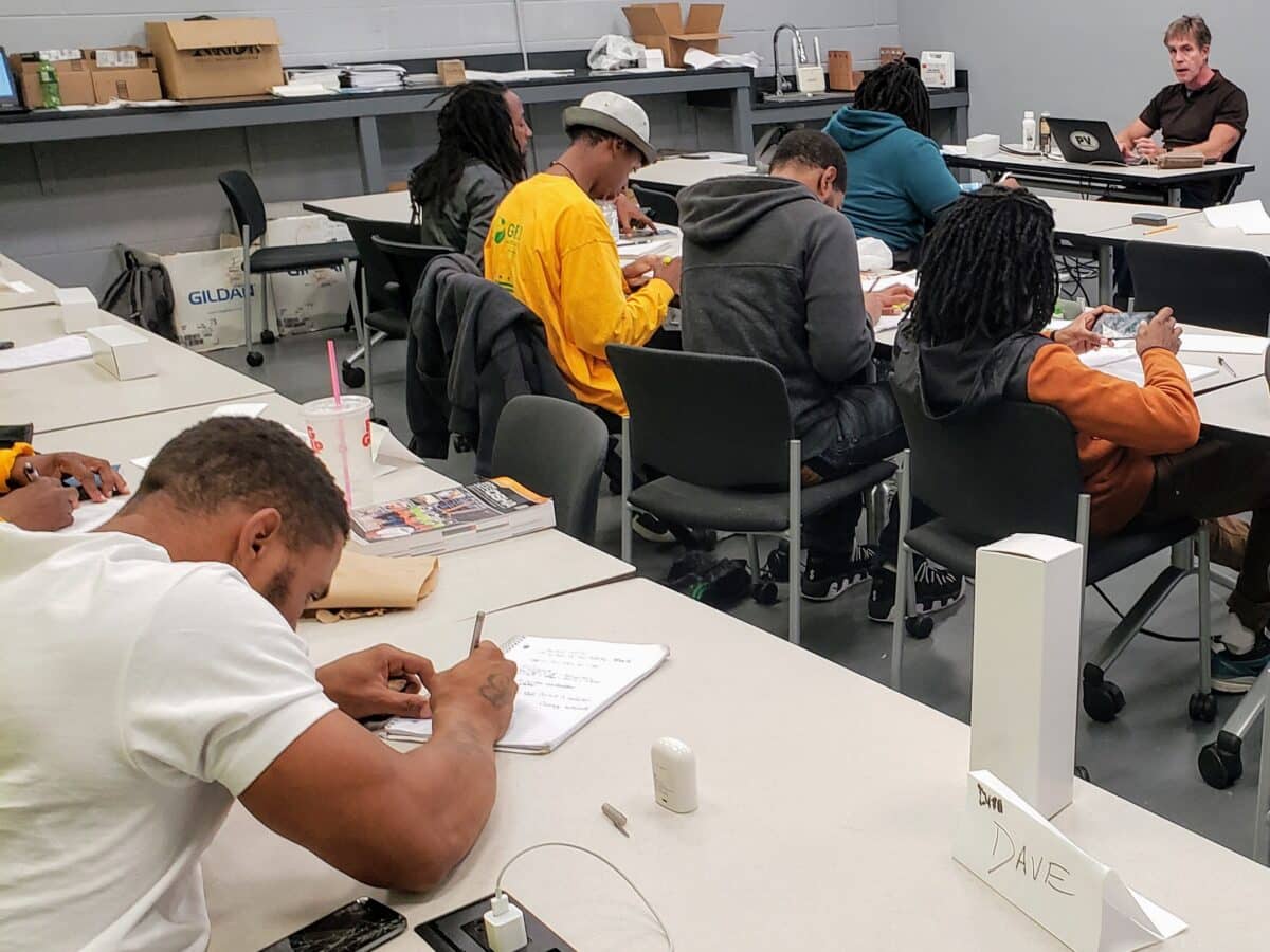 Students working at desks in a classroom with an instructor observing from the back of the room