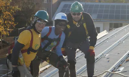 Three workers in safety gear on a rooftop with solar panels and building visible