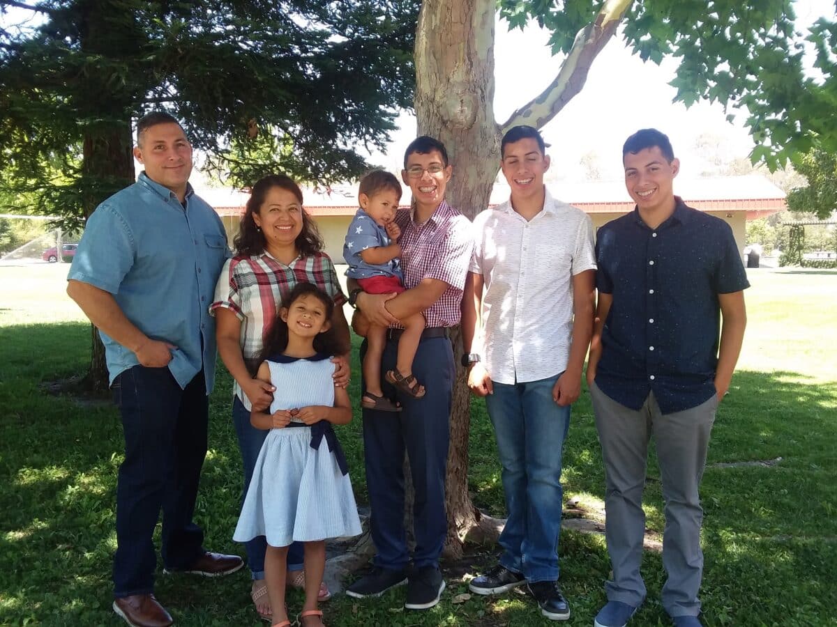Family of six adults and two children posing together under a large tree in a park