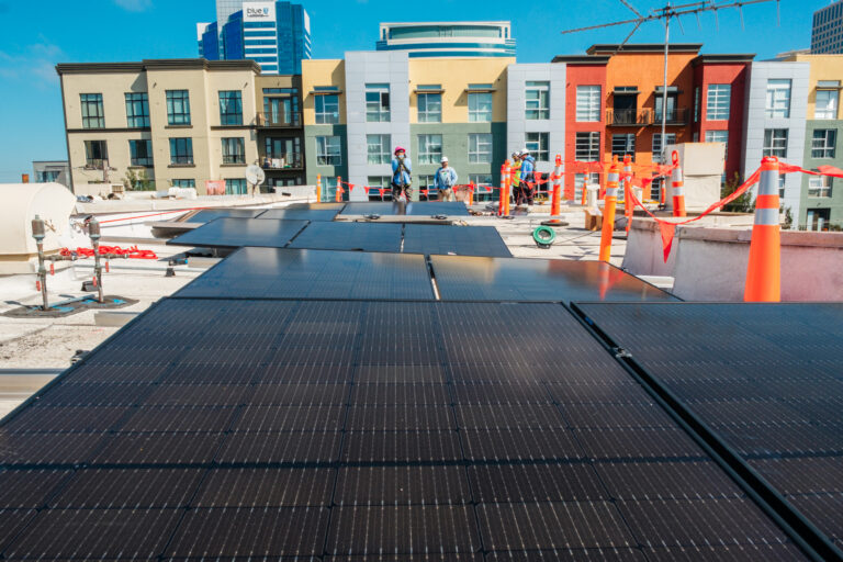 Solar panels being installed on a rooftop with colorful residential buildings in the background