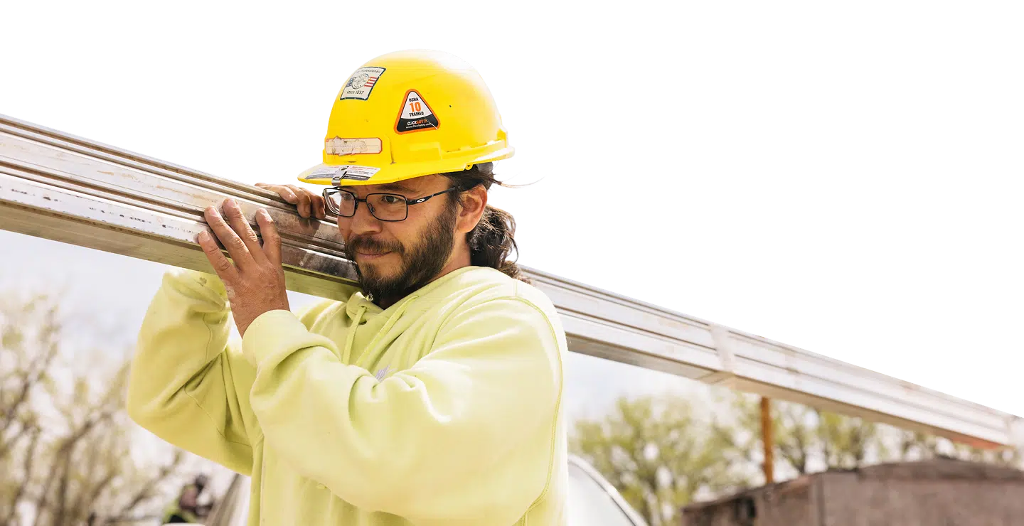 Construction worker in yellow safety helmet and high-visibility shirt carrying metal beam on shoulder