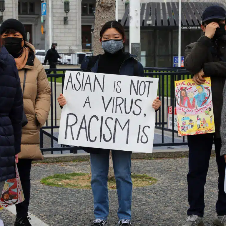 Protesters holding signs at rally, one reads "Asian is not a virus, racism is