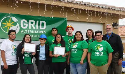 Group of people wearing green GRID Alternatives t-shirts posing together under a covered structure with icicle lights