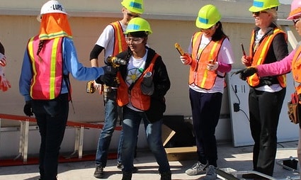Five construction workers in safety vests and hard hats gathered together on a job site
