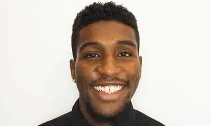 Smiling man with dark curly hair wearing a black shirt against a white background
