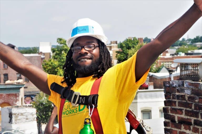 Devonte, a Solar Works DC trainee, puts his arms in the air while on the roof during a solar installation.