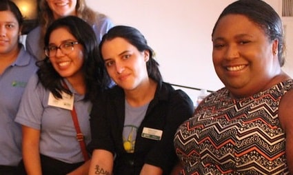 Group of five smiling people in casual and work attire at an indoor gathering