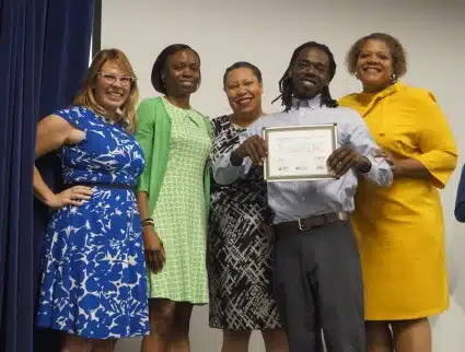 Trainee Daniel poses with the graduation speakers, Nicole Steele of GRID, Tarasa Lawrence of DOEE, Unique Morris-Hughes of DOES, and Deputy Mayor Courtney Snowden