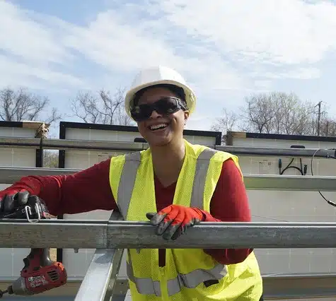 Woman in hard hat and safety vest smiling while working on construction site