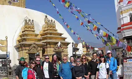 Group of tourists posing in front of golden Buddhist temple with colorful prayer flags overhead