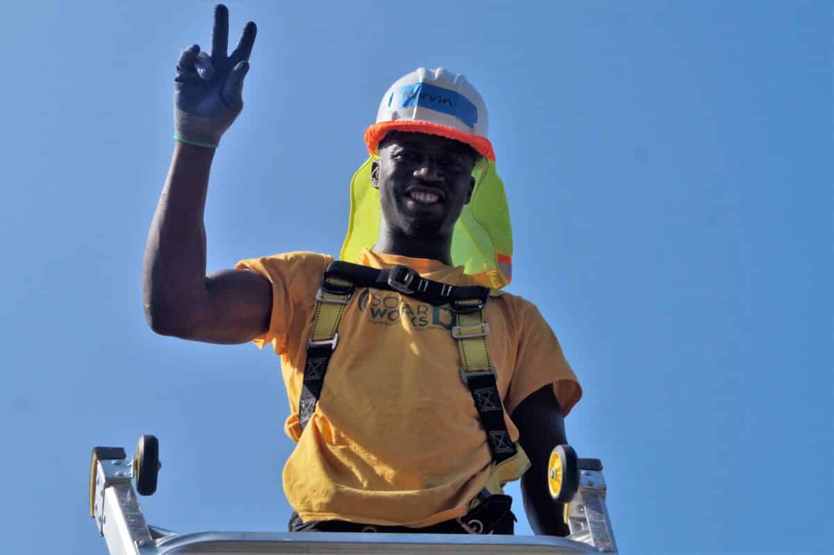Marvin, a Solar Works DC trainee, waves from the roof during a solar installation.