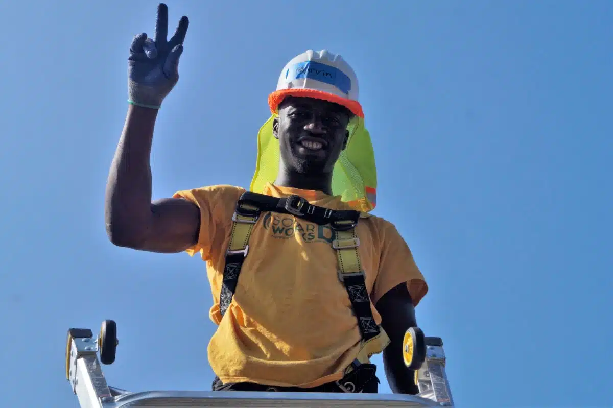 Marvin, a Solar Works DC trainee, waves from the roof during a solar installation.