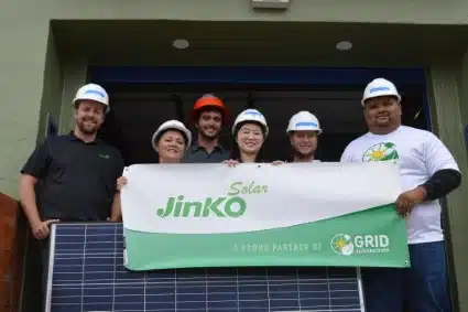Team holding Jinko Solar banner with solar panel installation