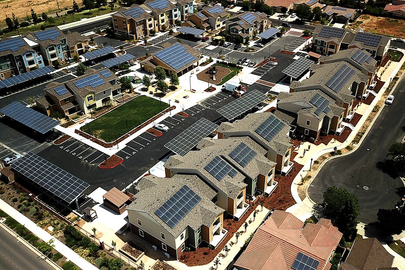 Aerial view of residential neighborhood with solar panels on rooftops and a parking lot with green space