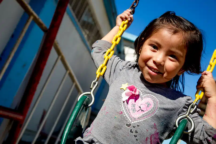 Young child smiling on a playground swing with yellow chain against blue sky