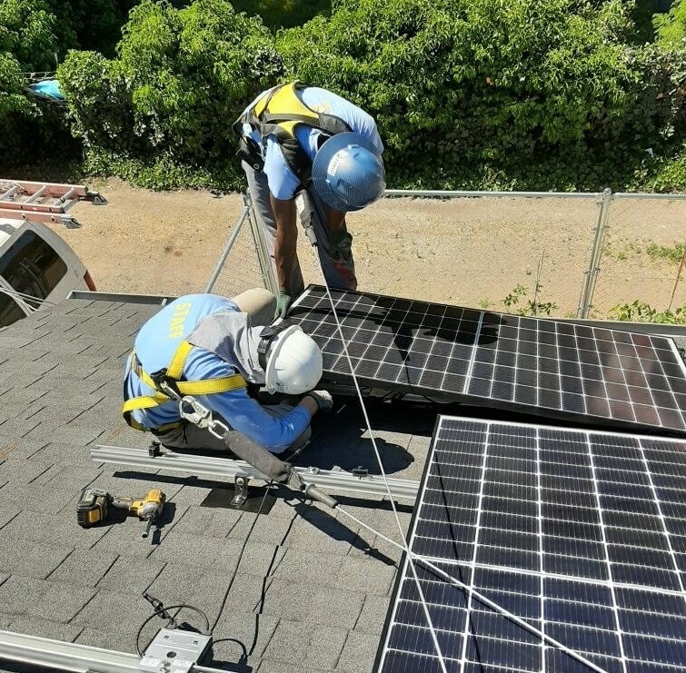 Two workers in safety gear installing solar panels on a residential roof on a sunny day