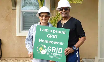 Two people wearing hard hats hold a green sign reading "I am a proud GRID Homeowner