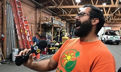 Man in orange shirt with sun logo holding red ladder in warehouse workshop