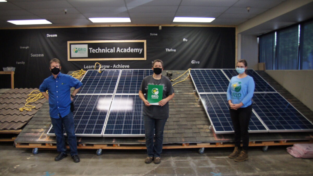 Three people stand with solar panels in GRID Technical Academy training facility