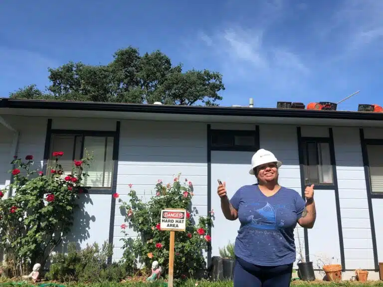 Woman in hard hat giving thumbs up in front of house under construction with blooming roses