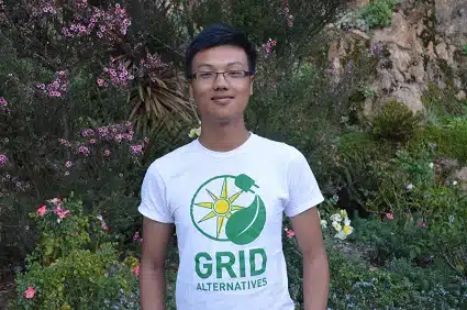 Person wearing GRID Alternatives t-shirt smiling in front of flowering vines