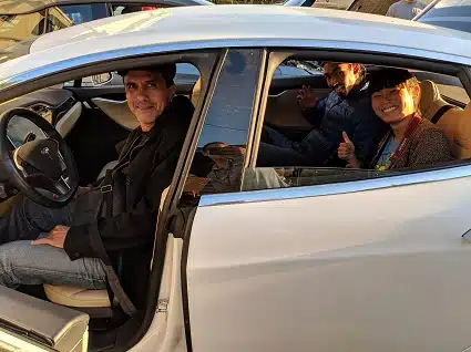 Man smiling in driver's seat of white electric vehicle with passengers visible in back seat