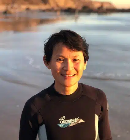 Young person in wetsuit at beach at sunset, smiling at camera