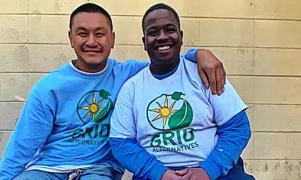 Two smiling men wearing matching blue AGRO International shirts pose together against a brick wall