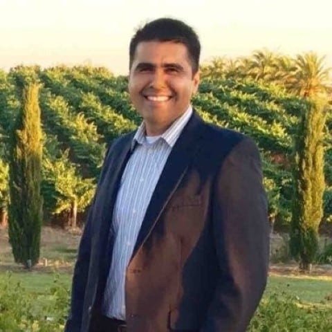 Man in brown blazer and blue shirt smiling in vineyard setting