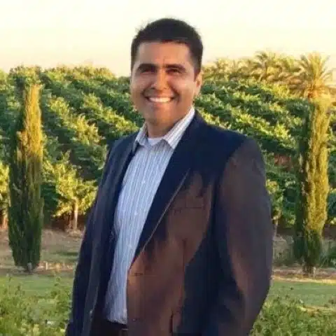 Man in brown blazer and blue shirt smiling in vineyard setting