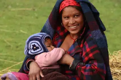Smiling young woman in colorful blankets holding a newborn baby outdoors