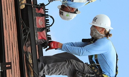 Construction worker in hard hat and safety gear installing electrical equipment on brick wall