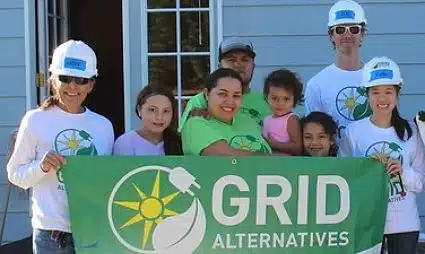 Group of volunteers in hard hats holding GRID Alternatives banner at community event