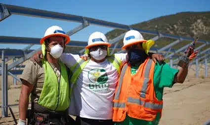Three construction workers in safety gear at solar panel installation site