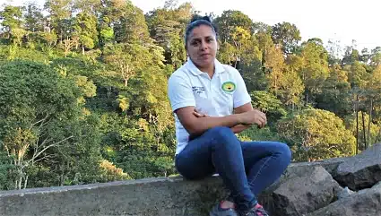 Woman in white shirt sitting on concrete ledge with forest background