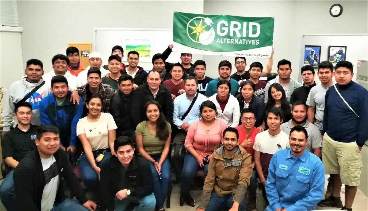 Large group of people posing together holding a green GRID Alternatives banner indoors