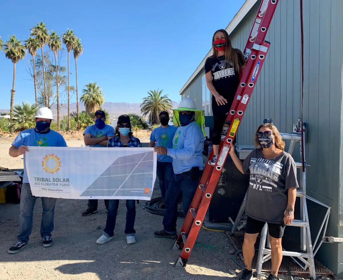 Group holding Tribal Solar Accelerator Fund banner at desert construction site with palm trees and red ladder