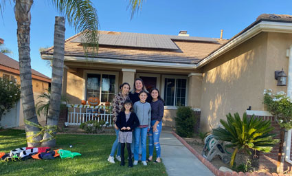 Family of five standing on walkway in front of single-story house with solar panels