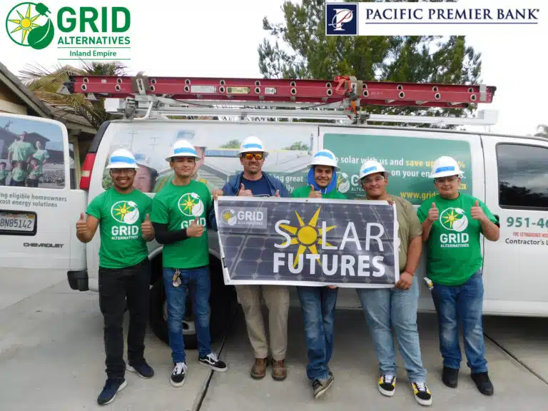 Six GRID Alternatives workers in green shirts and hard hats hold "Solar Futures" banner in front of company van