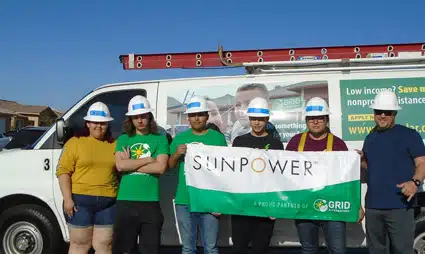 Team of volunteers in hard hats holding SunPower banner in front of van